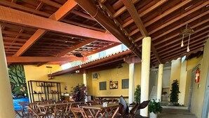 An indoor dining area with wooden tables and chairs, a tiled floor, and a ceiling with wooden beams. - Pousada Aconchego da Serra (Martins)
