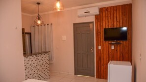 A hotel room with a bed, a television mounted on a wooden wall, a door, and a small refrigerator. - Pousada Aconchego da Serra (Martins)