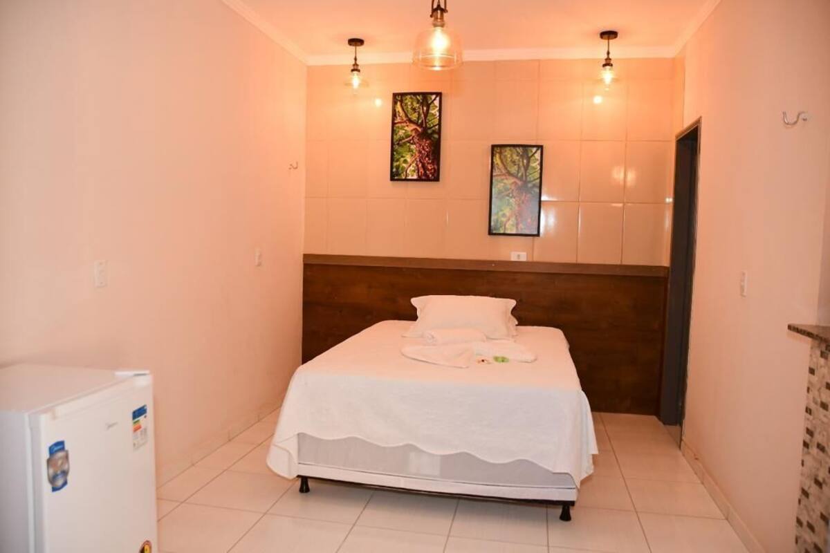 A small, neatly arranged bedroom with a single bed, a wooden headboard, and two wall-mounted light fixtures.
