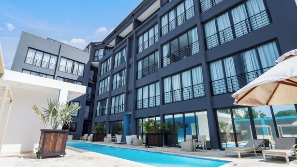 A modern building with a swimming pool, lounge chairs, and potted plants. - Cozy 1BR suite at Rizz Suites – GYM, Pool, A/C & Walk to Beach (Sosúa)