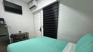 A room with a bed, a small table with chairs, a television, and an air conditioning unit.