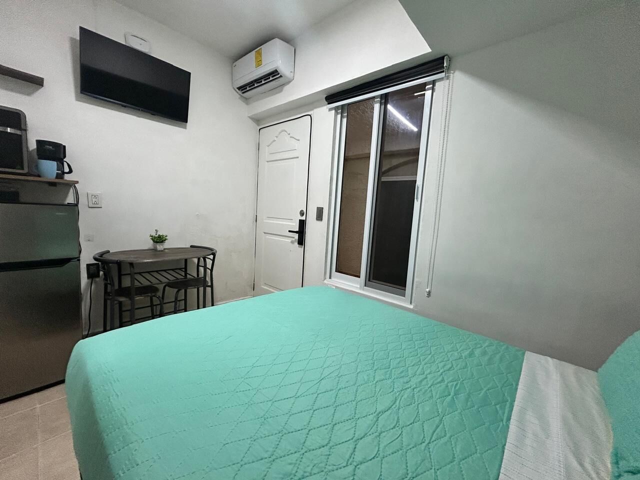 A bedroom with a bed, a desk, a chair, a TV, and a sliding door.