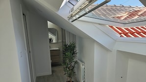 Un pasillo estrecho con tragaluces, un radiador y una planta en maceta.