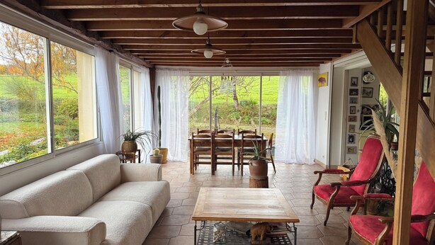 A cozy living room with a sofa, a wooden coffee table, and red chairs. There is a dining table with chairs in the background. - Le Jardin Des Dames Lavandes (Ganties)