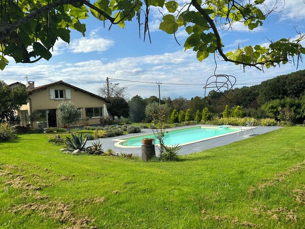 Une maison avec une piscine, entourée d’une pelouse bien entretenue et de diverses plantes.