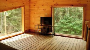 A cabin with wooden walls and floors, a television on a stand, and large windows offering a view of the forest. - Peaceful Pines (South Bloomingville)