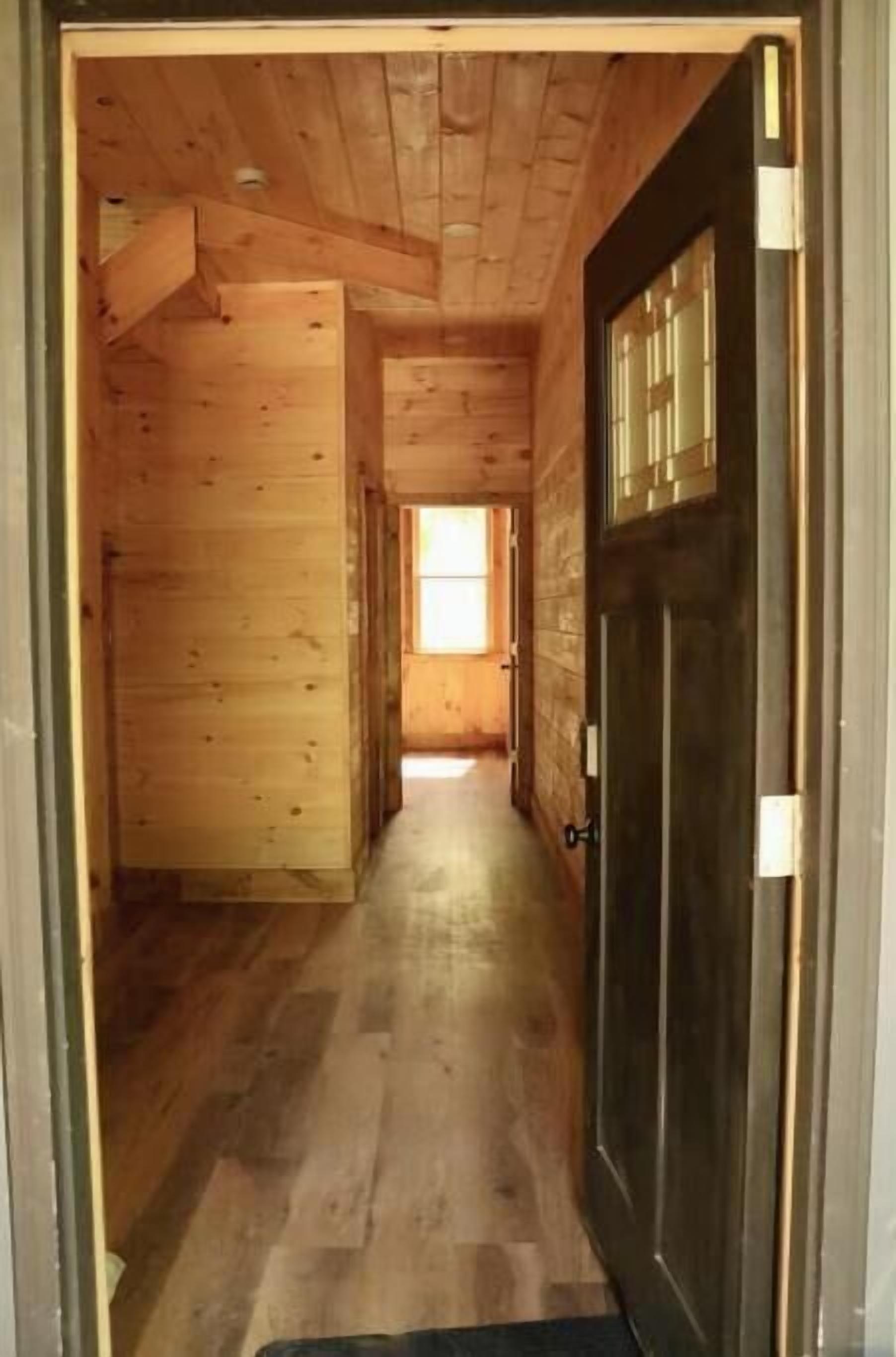 A wooden interior hallway with a dark door and a window at the end.