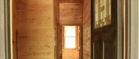 A wooden interior hallway with a dark door and a window at the end.