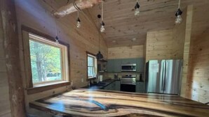 A wooden cabin interior with a kitchen area, a large island with bar stools, and hanging light fixtures. - Peaceful Pines (South Bloomingville)
