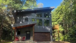 A modern two-story cabin with a large garage, surrounded by a forest. - Peaceful Pines (South Bloomingville)