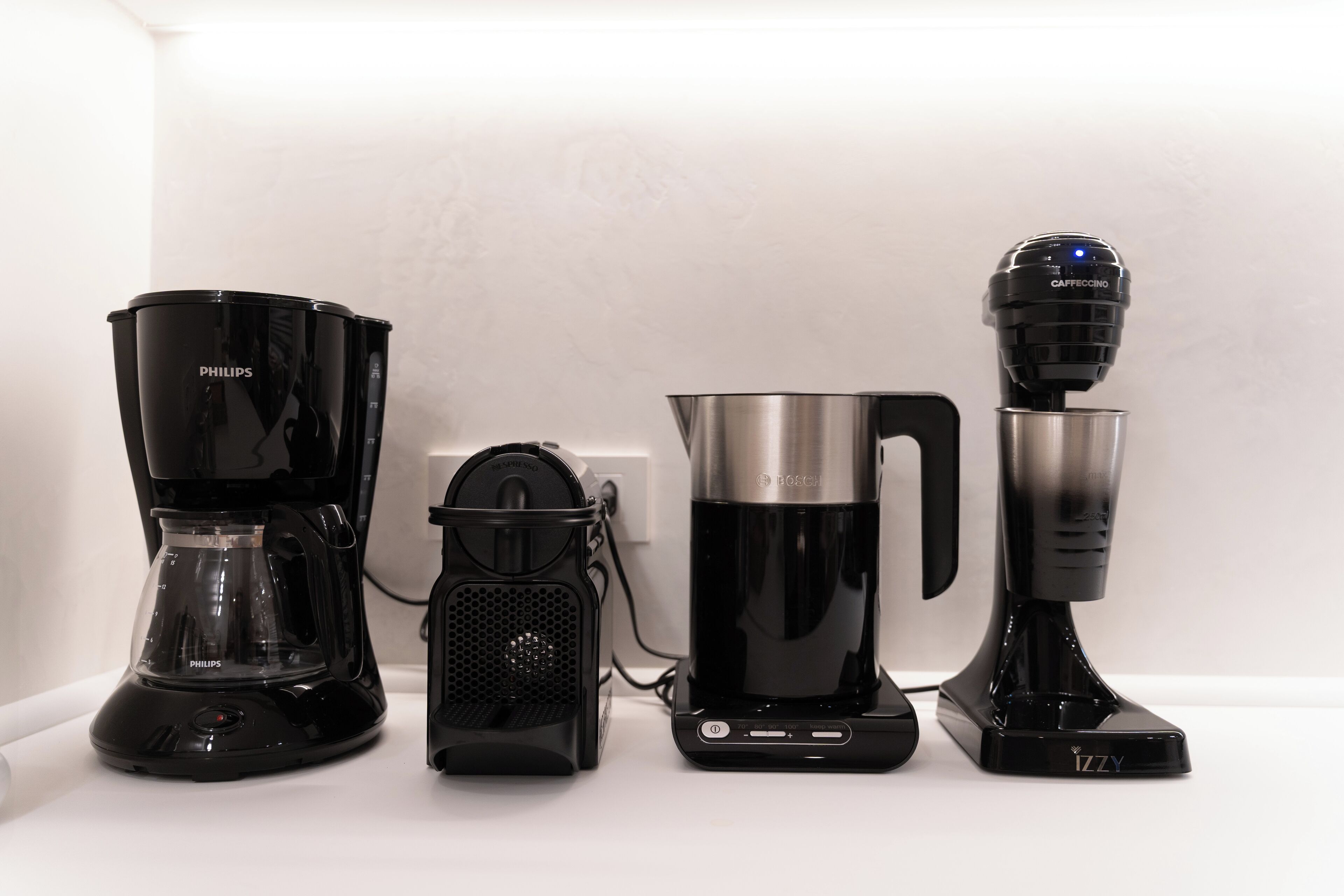Four coffee makers on a white countertop.