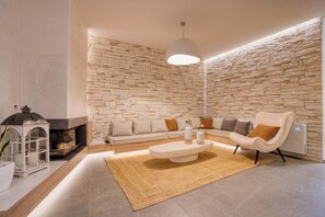 A modern living room with a stone wall, a fireplace, a sofa set, a coffee table, and a lamp. - Citrine  - An Elegant Escape, where luxury, comfort, and style meet tranquility (Thymiana)