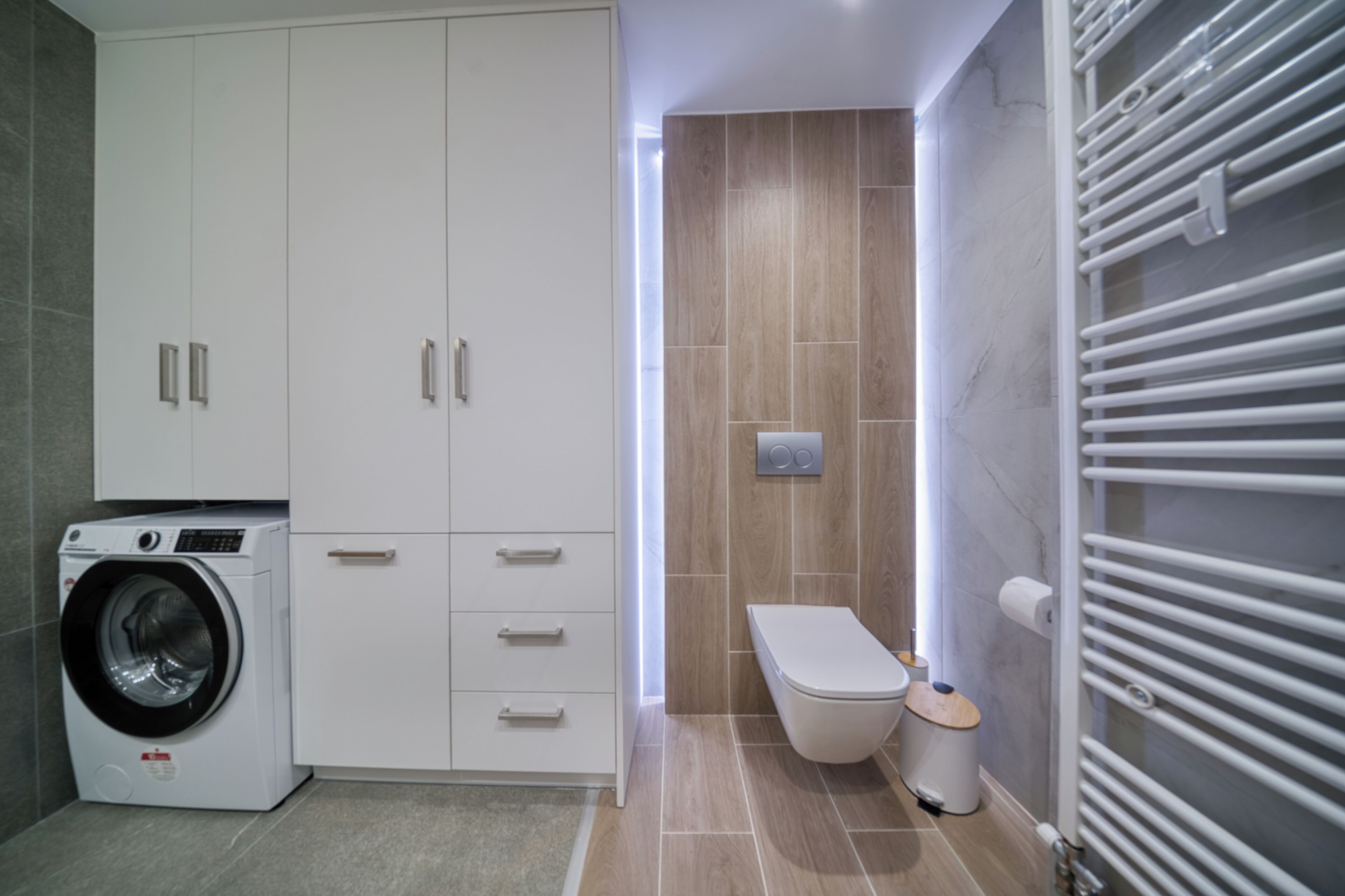 A modern bathroom with a built-in washing machine, a toilet, and a towel rack.