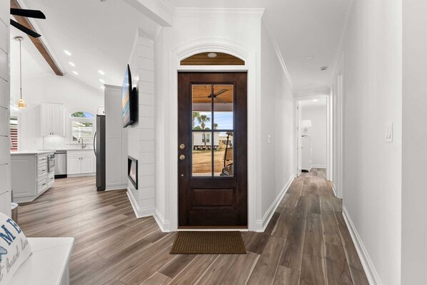 A modern kitchen with white cabinetry, a wooden floor, and a dark wooden door with a window.
