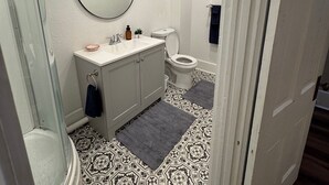A bathroom with a white vanity, a round mirror, a toilet, and patterned floor tiles.