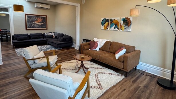 A spacious living room with a sofa, armchairs, and a coffee table. There is a large painting on the wall and a floor lamp.
