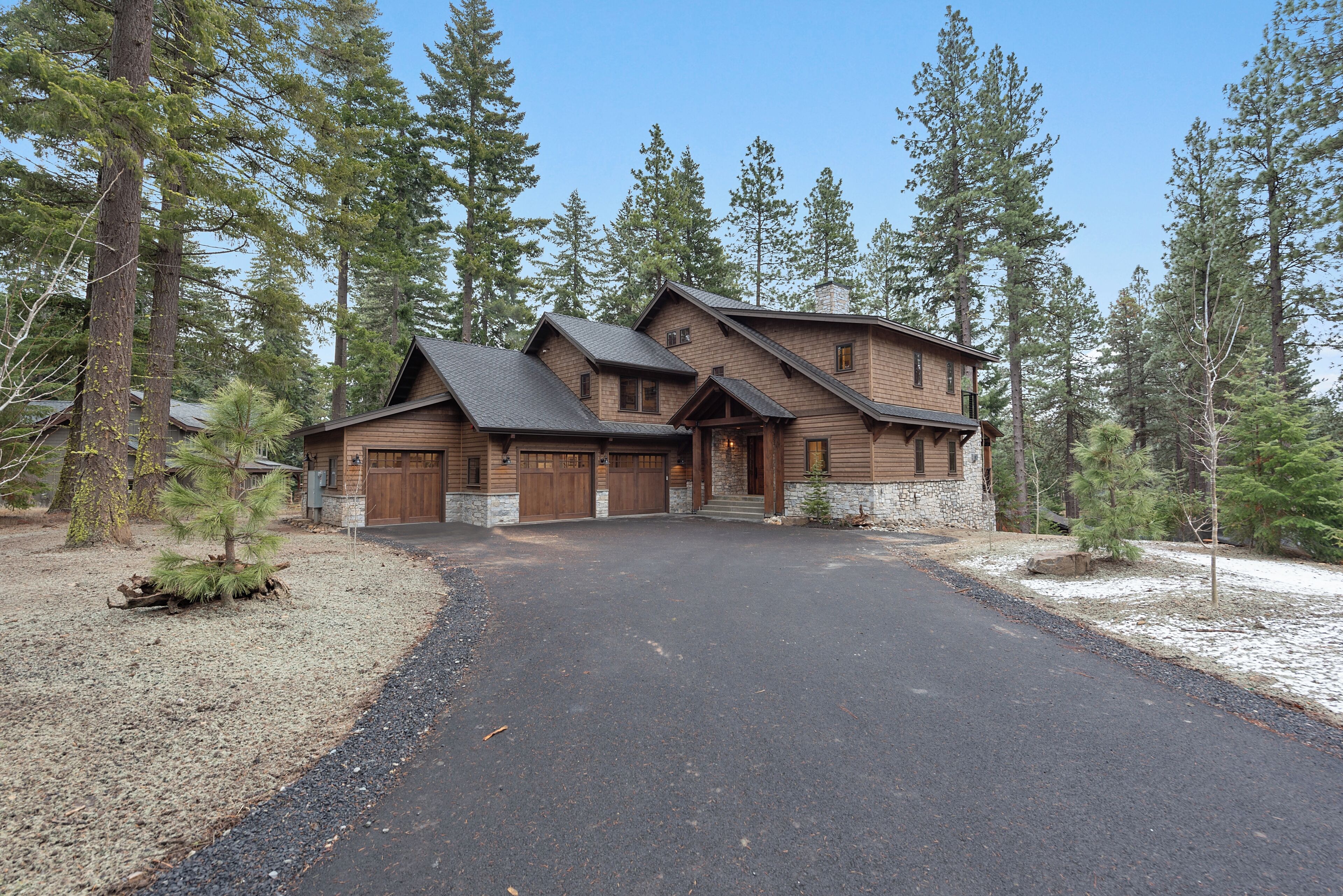 A two-story log cabin with a stone foundation, a garage, and a driveway leading to the entrance.