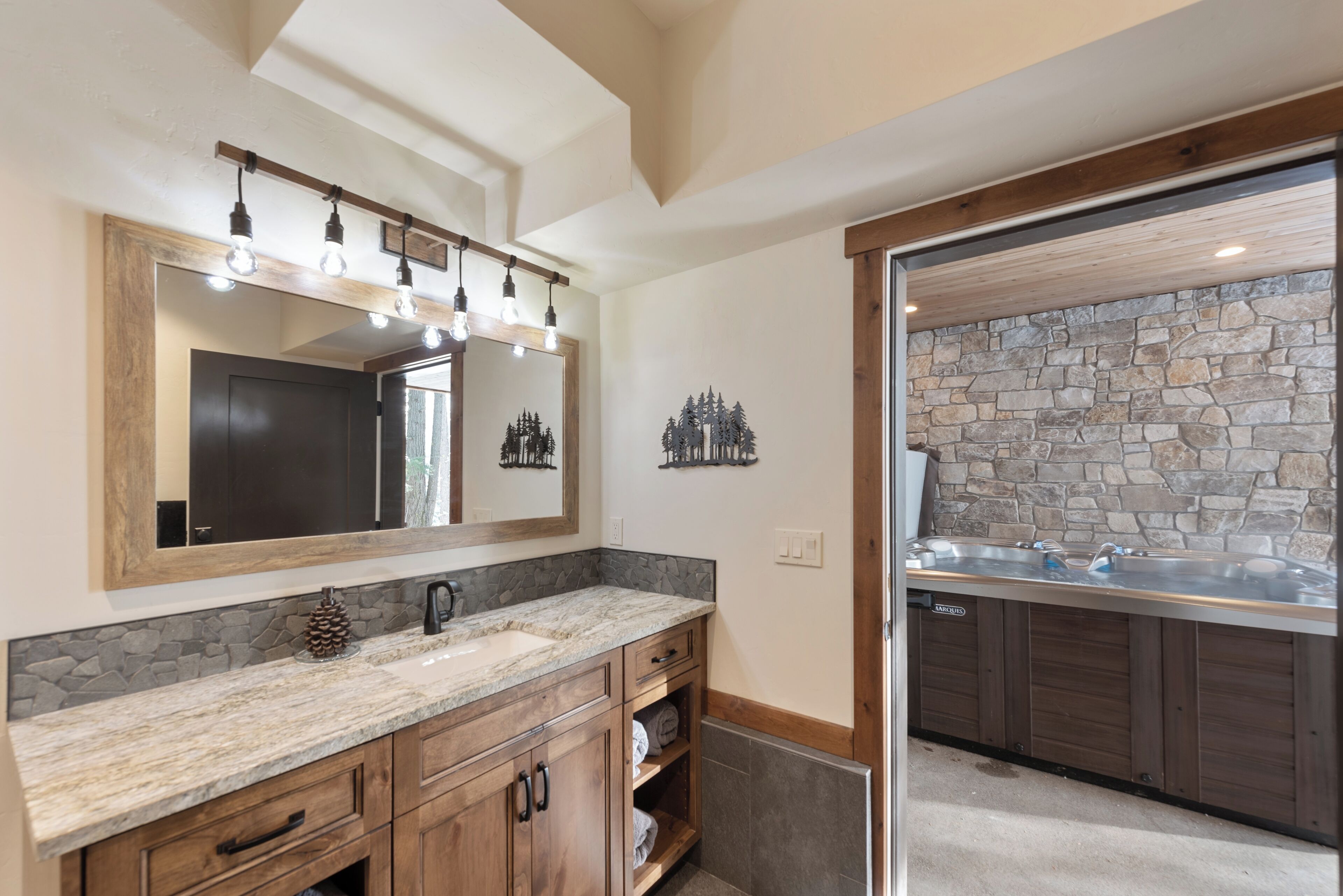 A bathroom with a stone wall, a large mirror, wooden cabinets, and a sink.