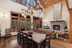 A spacious living area with a stone fireplace, wooden dining table, and large windows. - Luxury 5 Suite Suncadia Golf Course Hm w Hot Tub, Sauna, Game & Theater Level (Cle Elum)