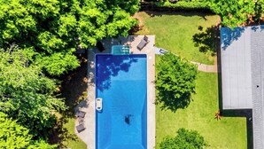 Ein Luftbild eines Wohnhauses mit Schwimmbecken, umgeben von üppiger Vegetation und einem gepflegten Rasen.