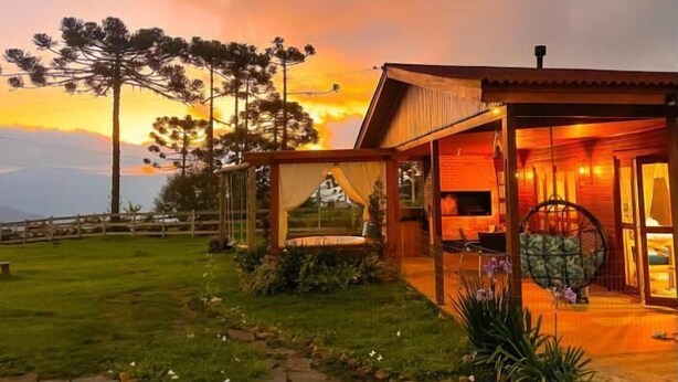 A wooden cabin with a porch, surrounded by a well-maintained lawn and trees, set against a sunset sky.
