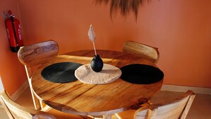 A round wooden table with a black vase and a woven placemat, surrounded by wooden chairs.