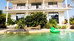 A two-story building with a balcony, a swimming pool, and tropical landscaping.