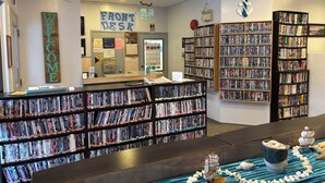 A library with a 'Welcome' sign, a 'Front Desk' sign, and multiple book shelves. - LEISURE INN (Temiskaming Shores)