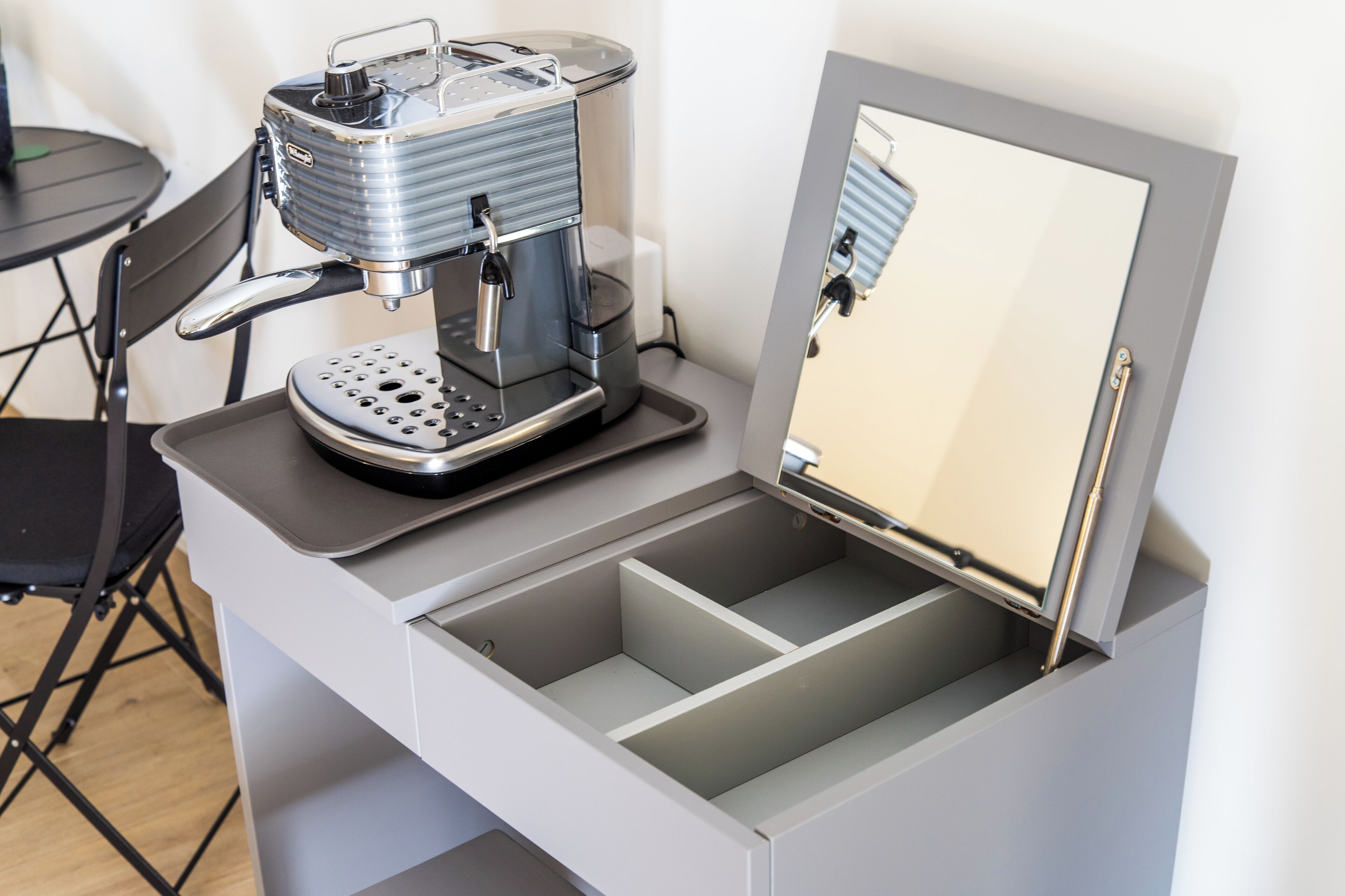 Une petite cuisine équipée avec une machine à café, un miroir et une chaise pliante.