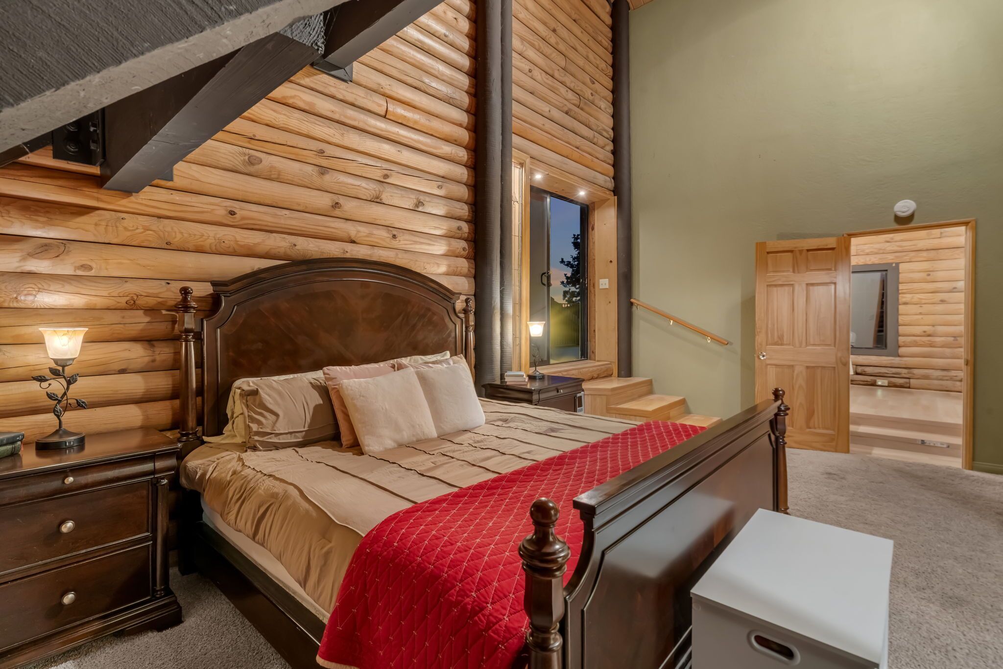 Ein schlafzimmer im Chalet-Stil mit einem hölzernen Bett, Nachttischen und einer roten gesteppten Bettdecke.