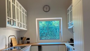 Een compacte keuken met witte kastjes, een ingebouwde oven en een raam met uitzicht op een groen landschap.