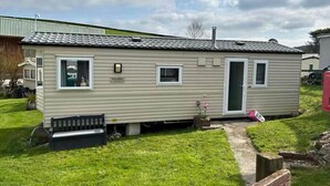A mobile home with a small porch, a bench, and a pathway leading to the entrance. - Popular resort- with indoor and outdoor pool (Newquay)