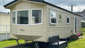 A mobile home with a front porch, a small deck, and a garden area with flowers. - Popular resort- with indoor and outdoor pool (Newquay)