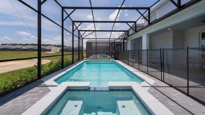 A rectangular swimming pool with a glass enclosure, surrounded by a brick patio and a metal fence. - New Jungle Adventure 9BR Villa by Disney (Davenport)
