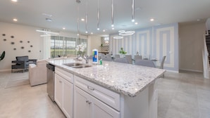 A modern kitchen with a granite countertop, white cabinetry, and pendant lighting. - New Jungle Adventure 9BR Villa by Disney (Davenport)