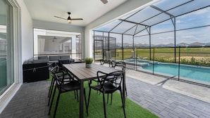 A modern outdoor patio with a pool, seating area, and large windows offering a view of the countryside. - New Jungle Adventure 9BR Villa by Disney (Davenport)