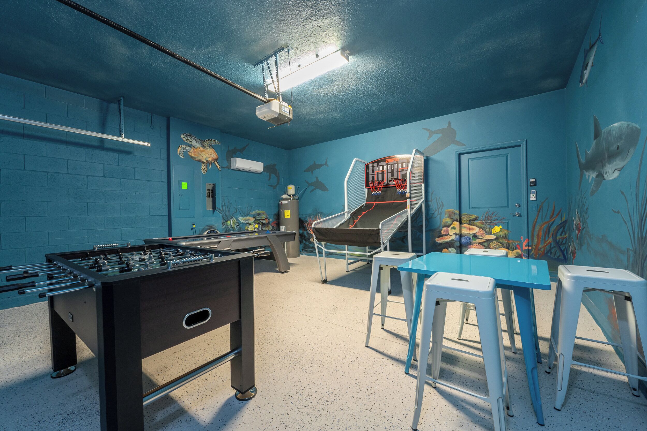 A room with a foosball table, a pool table, and a mural of sharks and marine life on the walls.