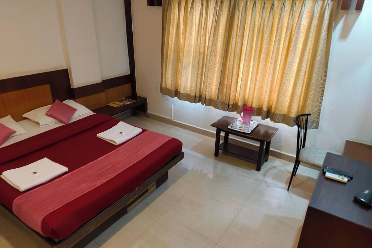 A hotel room with a bed, a small table, a chair, and a desk with a remote control.