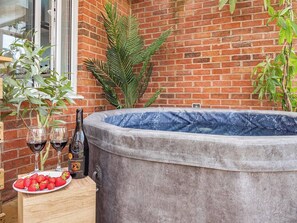 A hot tub next to a brick wall with a wooden table holding wine glasses and strawberries. - Chic Riverside Retreat Salford 4bd + free parking (Salford)