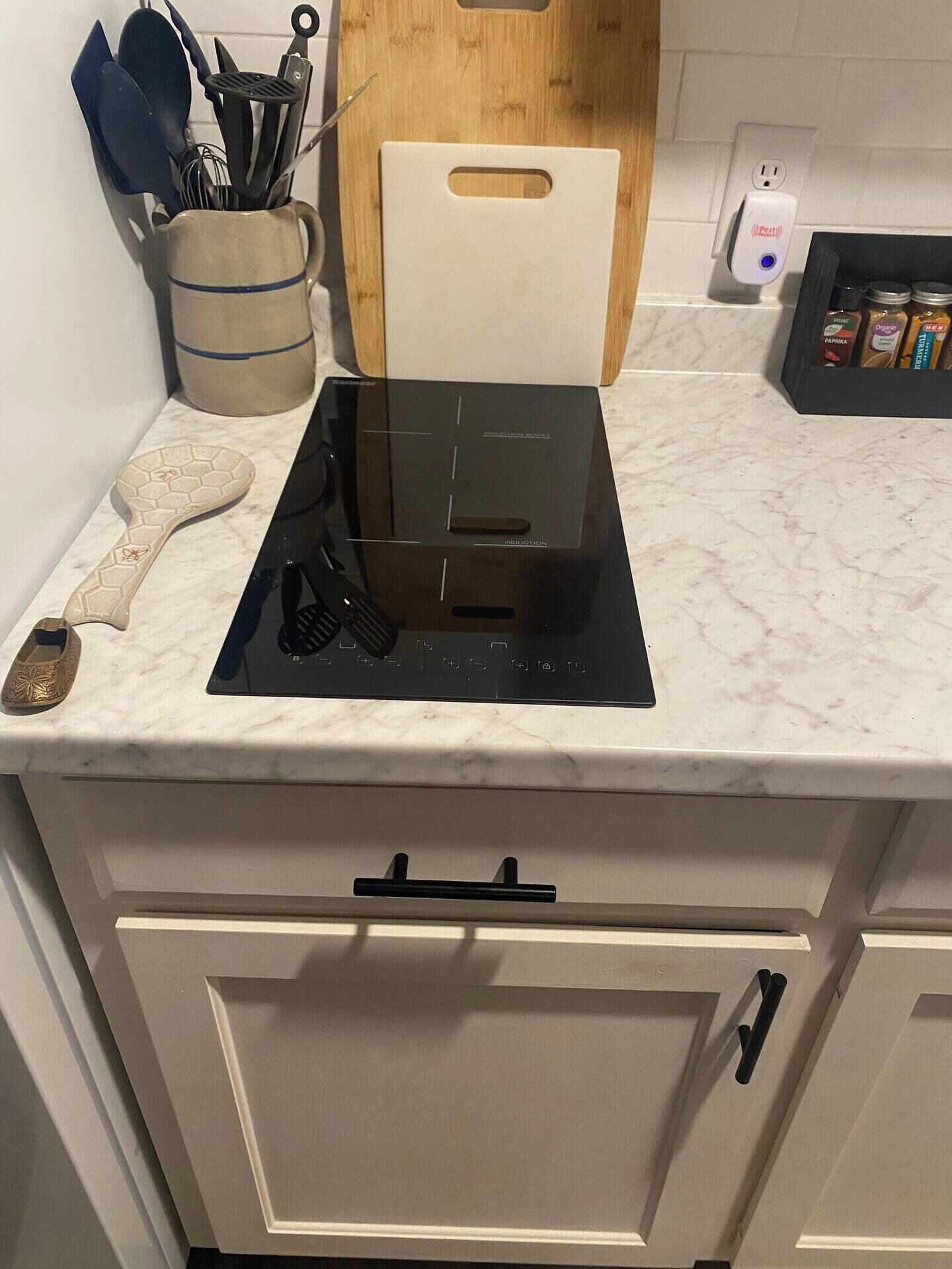 A kitchen with a black induction cooktop, a cutting board, and a spice rack.