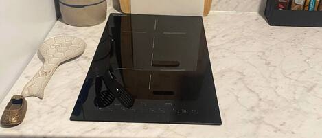 A kitchen with a black induction cooktop, a cutting board, and a spice rack.