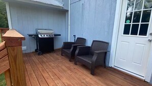 Een terras met een barbecue, rieten stoelen en een witte deur.