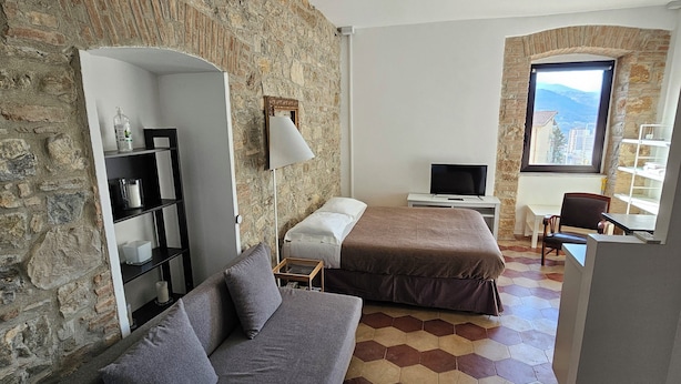 A room with a stone wall, a sofa, a bed, a TV, and a window with a view.
