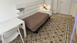 A small, neatly arranged room with a bed, a desk, a wardrobe, and a patterned floor. - Single Room with Shared Bathroom and Private Parking in Loco (Potenza)