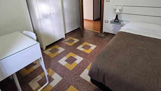 A bedroom with a bed, a desk, a wardrobe, and a patterned carpet. - Single Room with Shared Bathroom and Private Parking in Loco (Potenza)