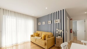 A modern living room with a yellow sofa, a white table, and a striped wall. - Casa das Sardinhas - 2 minutes walk from the beach (Nazaré)