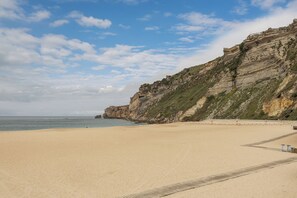 Ein Strand mit einer felsigen Klippe, einem Sandufer und einem klaren Himmel.
