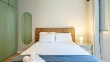 Un dormitorio ordenado con una cama, una mesita de noche, un armario verde y un espejo adosado a la pared.