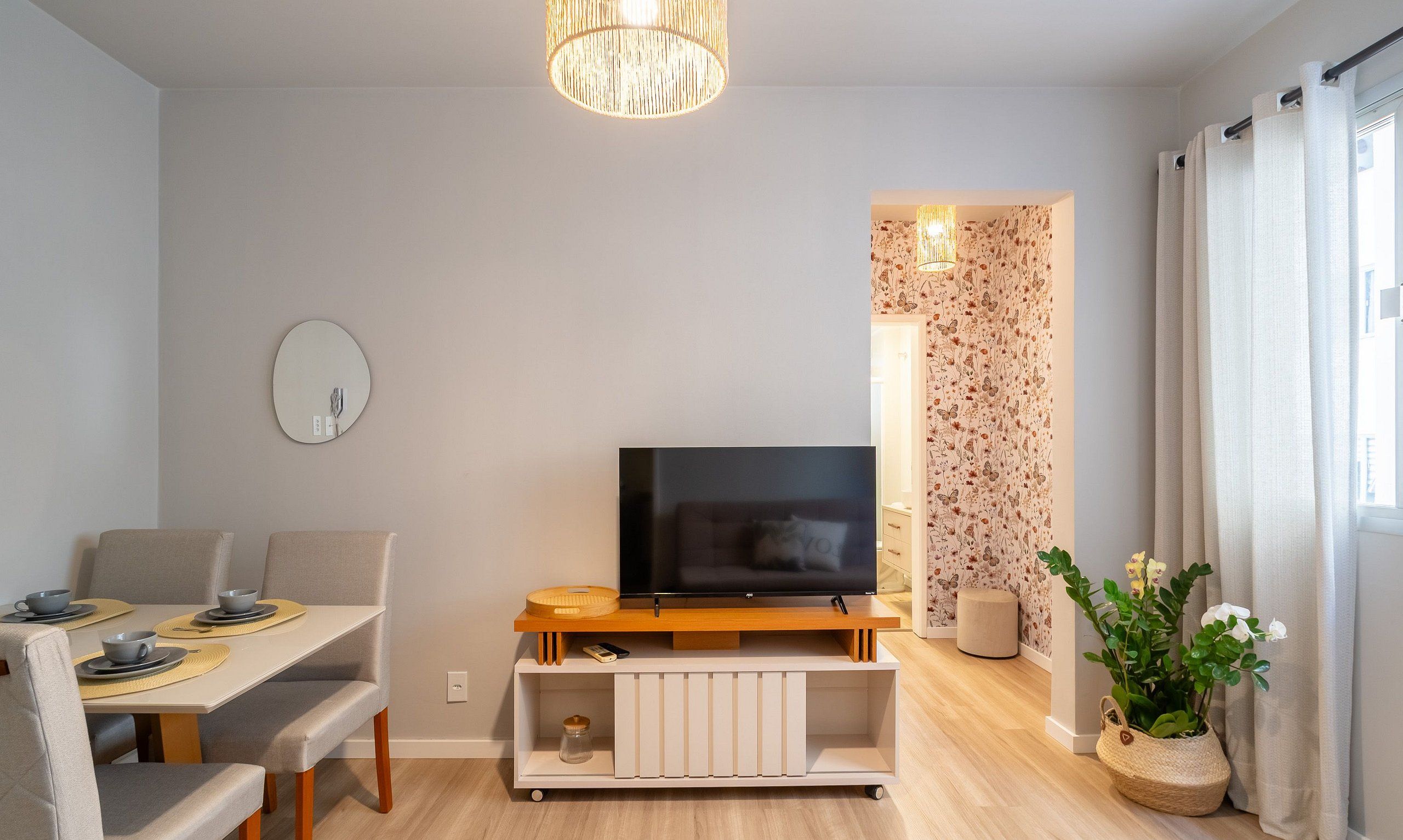 A modern living room with a flat-screen TV, a dining area with a table and chairs, and a decorative plant.