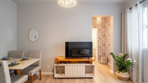 A modern living room with a flat-screen TV, a dining area with a table and chairs, and a decorative plant. - Apto Central a 600m da Beira-Mar Norte SGS0106 (Florianópolis)